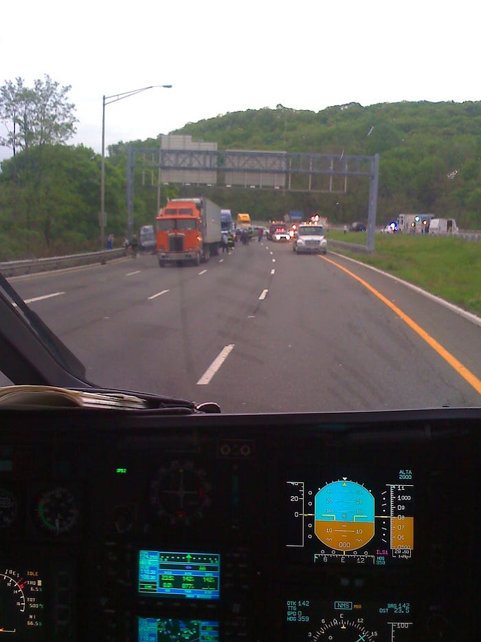 View from inside a medevac helicopter after landing on Route 80 in New Jersey, showing emergency vehicles and traffic stopped ahead. Helicopter instruments are visible in the foreground, emphasizing the precision required for a safe landing.