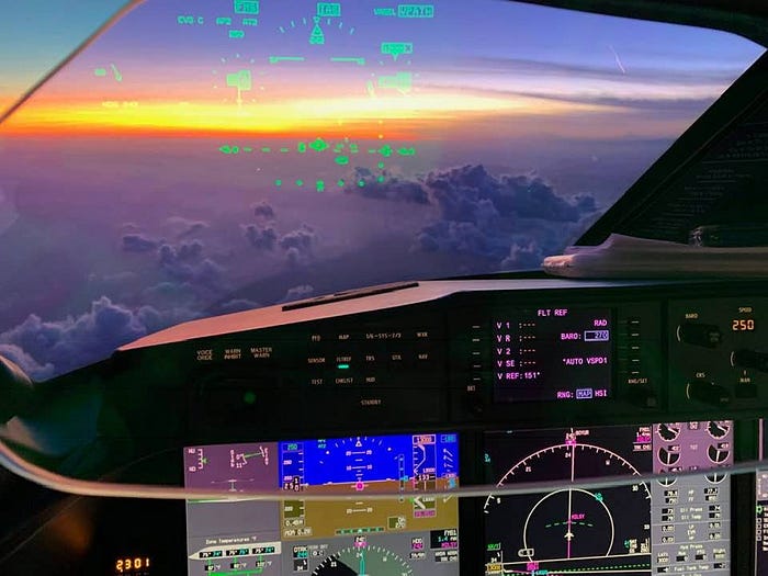 Cockpit view from a jet in flight, with the sun rising over a sea of clouds. The sunlight beams across the horizon, creating a peaceful yet powerful scene.